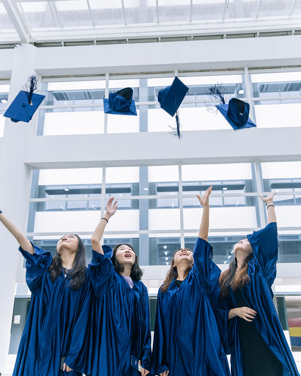 Four female OFS High School graduates throwing their graduation caps in the air in OFS Atrium