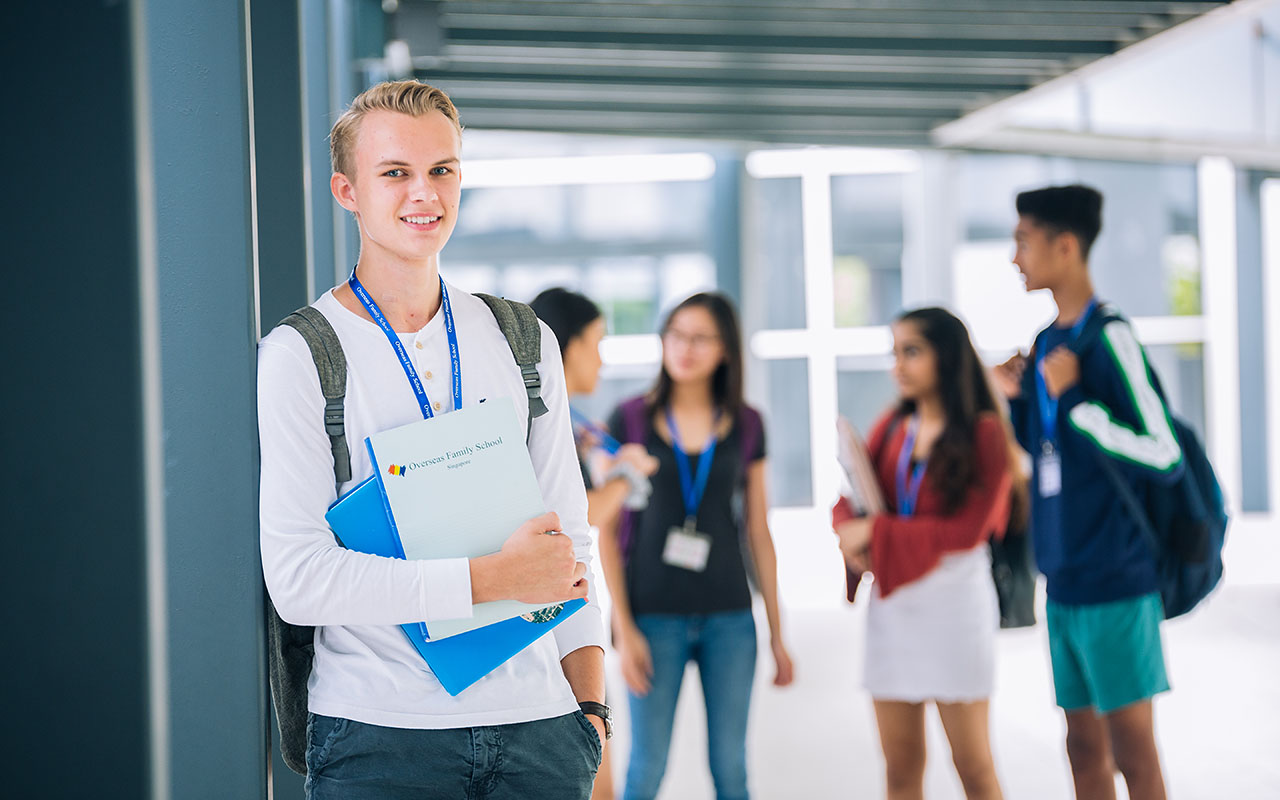 A male OFS Senior High School students standing and leaning on a pillar on the walkway while four others chatting in the background