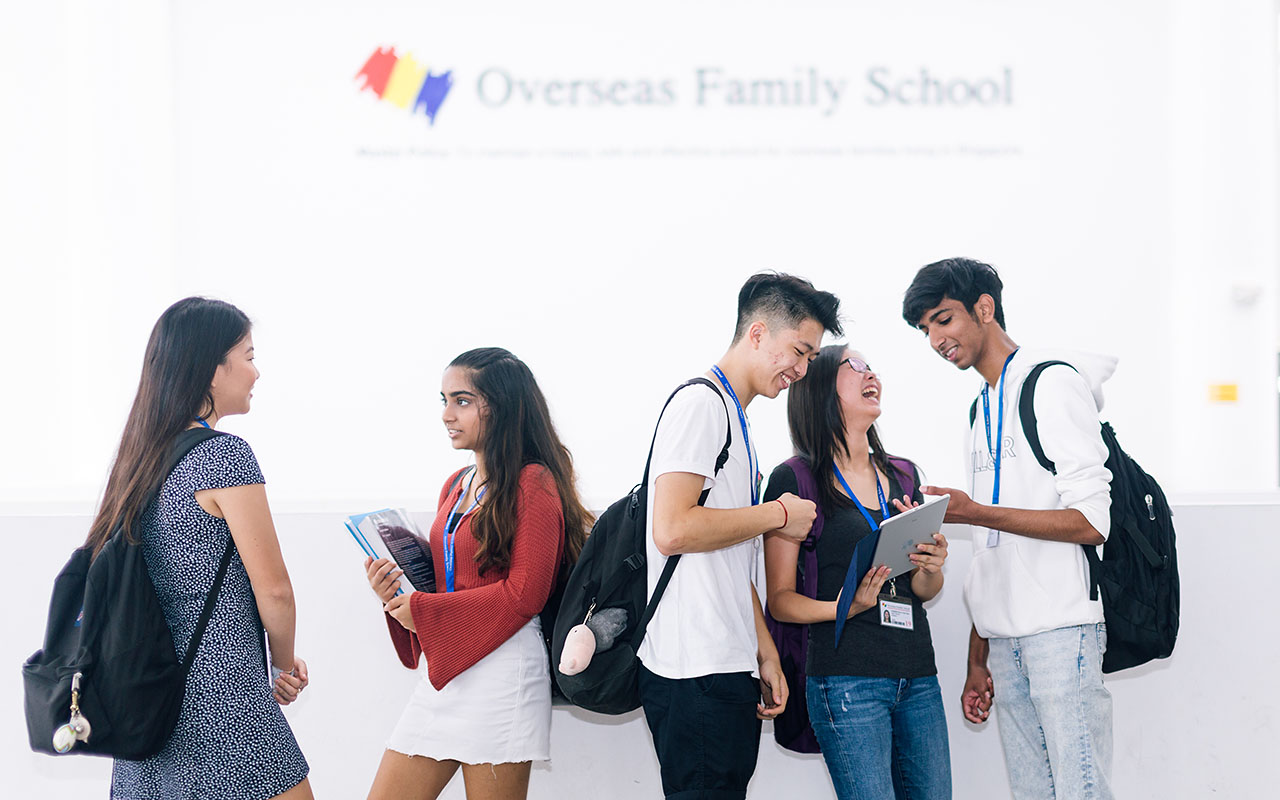 A group ofs OFS Senior High School students conversing in the Atrium with OFS logo in the background
