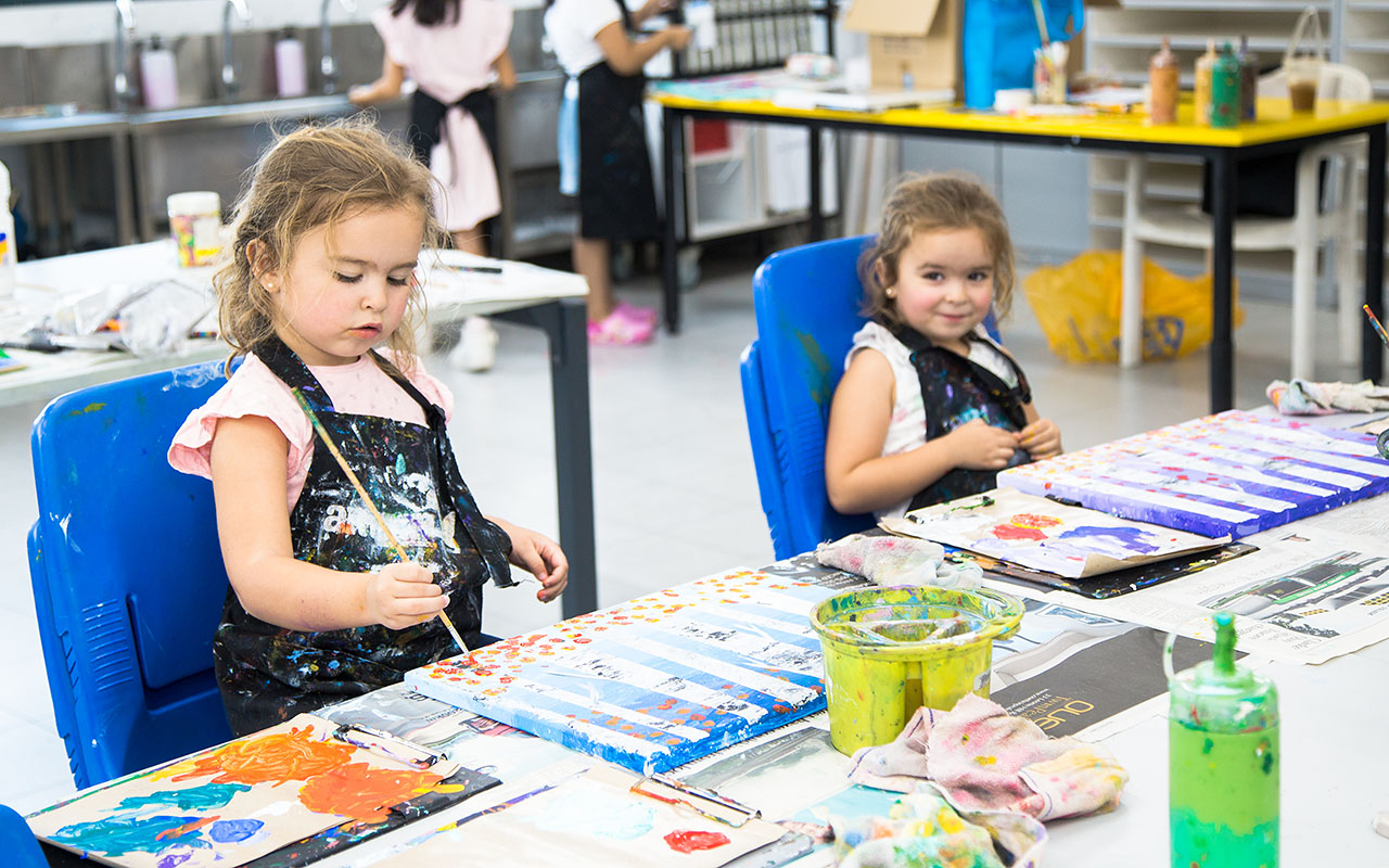 Two female OFS Kindergarten students painting on canvases during art enrichment class in the art studio