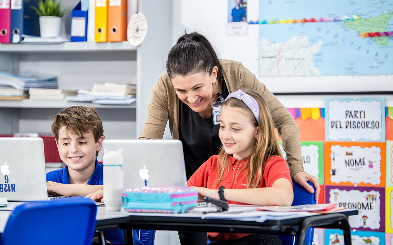 A female OFS mother tongue teacher smiling while teaching a couple of Elementary School students during mother tongue lesson