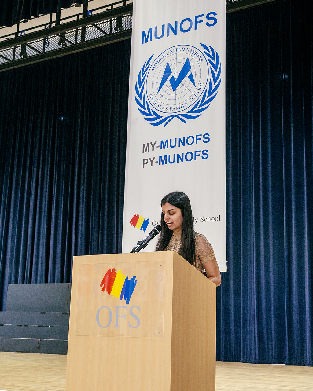 A female OFS High School student giving speech behind a podium in auditorium during OFS Model United Nations (MUNOFS)