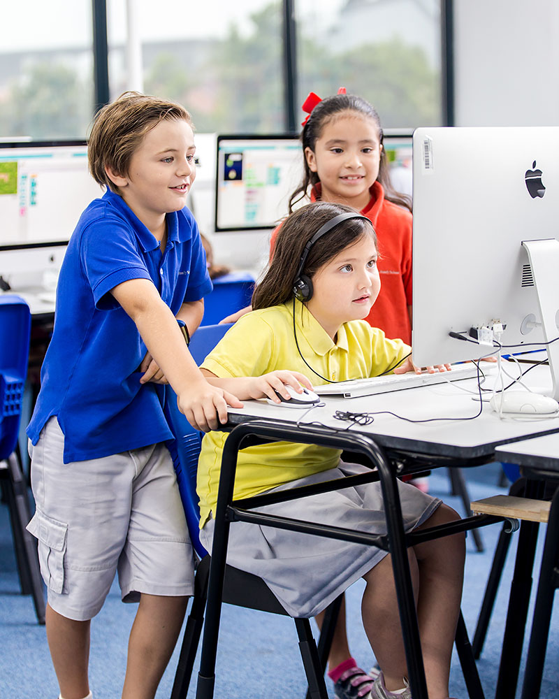 A female OFS Elementary School student using a computer while two other students watch from behind